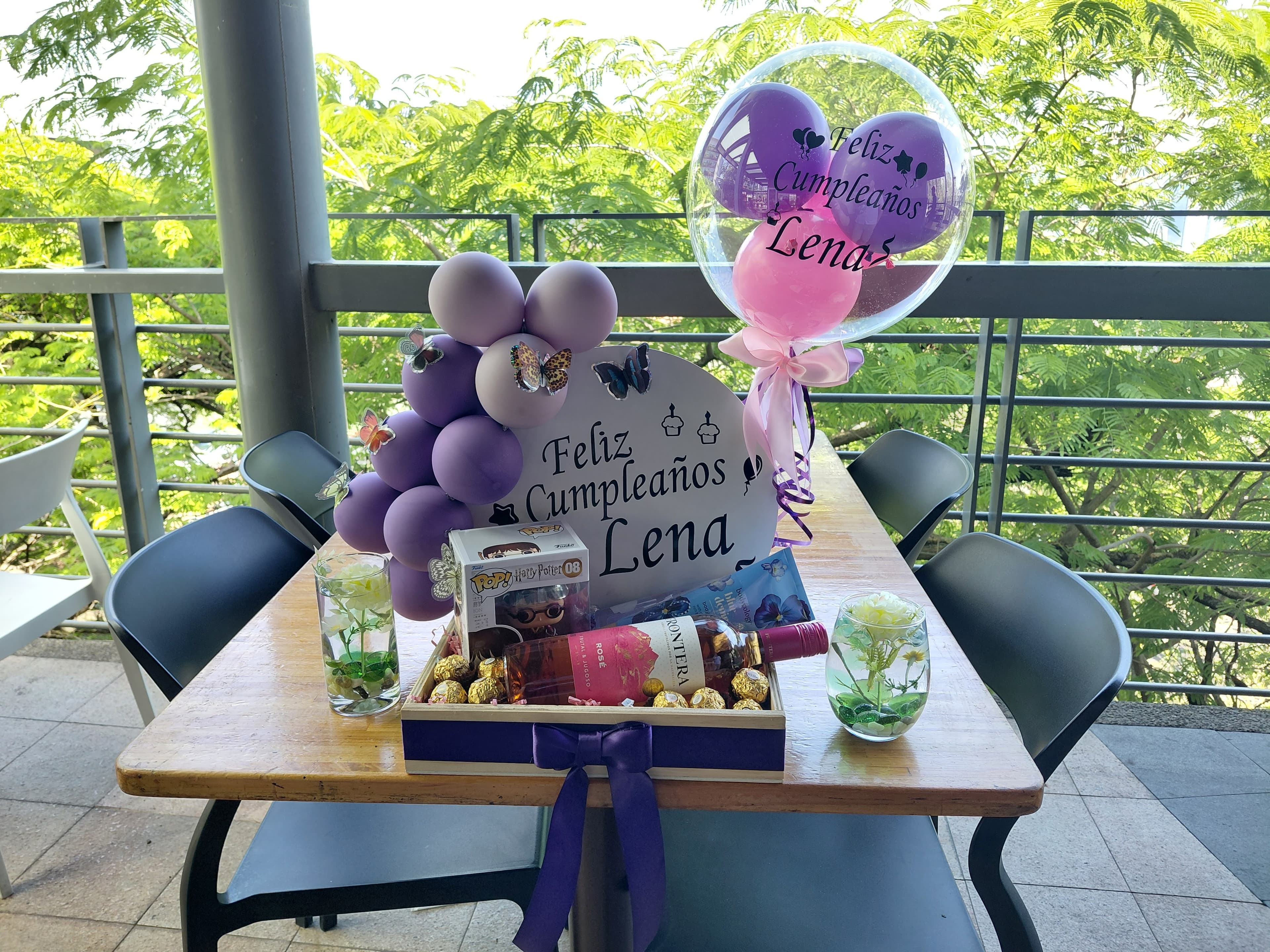 Mesa decorada con globos morados, rosa y un arreglo regalo con cupcake y globo burbuja personalizado